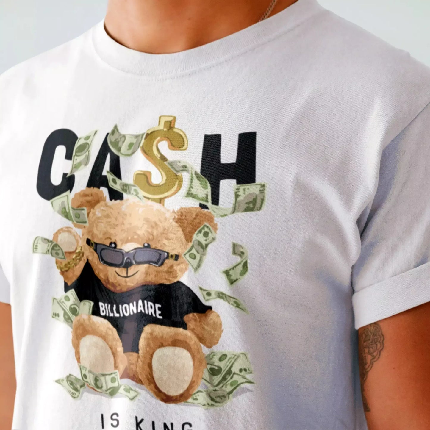 A white t-shirt featuring a teddy bear wearing sunglasses and a Billionaire shirt, surrounded by dollar bills – ένα λευκό t-shirt με αρκούδο που φοράει γυαλιά και μπλουζάκι Billionaire, περικυκλωμένος από χρήμα