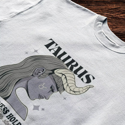 Elegant Taurus woman design printed on a white t-shirt, paired with bold typography “Her stillness holds” – Σχέδιο κομψής Ταυρίνας σε λευκό μπλουζάκι, με έντονη τυπογραφία “Her stillness holds