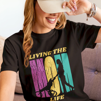 New mom wearing a black "Living The Mom Life" t-shirt while pushing baby stroller in park / Νέα μαμά φοράει μαύρο μπλουζάκι "Living The Mom Life" ενώ σπρώχνει καροτσάκι στο πάρκο
